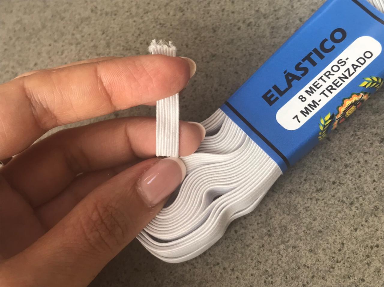 Hand holding a white elastic band package labeled “ELASTICO” on a beige surface