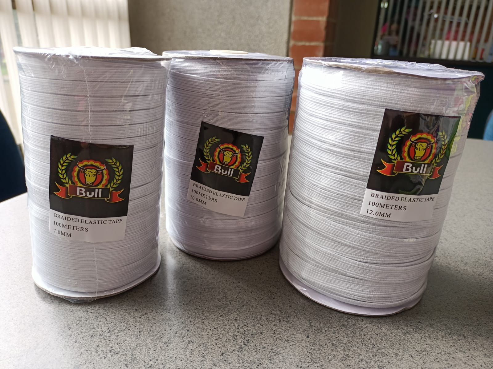 Three white rolled items with printed labels, stacked on a speckled countertop near a window