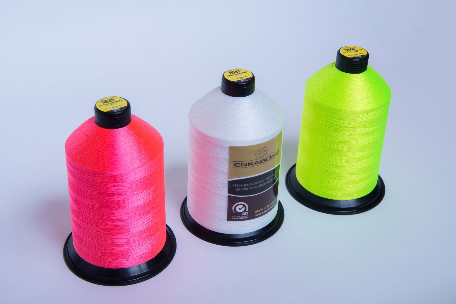 Three spools of thread: bright pink, white, and neon yellow on a light background