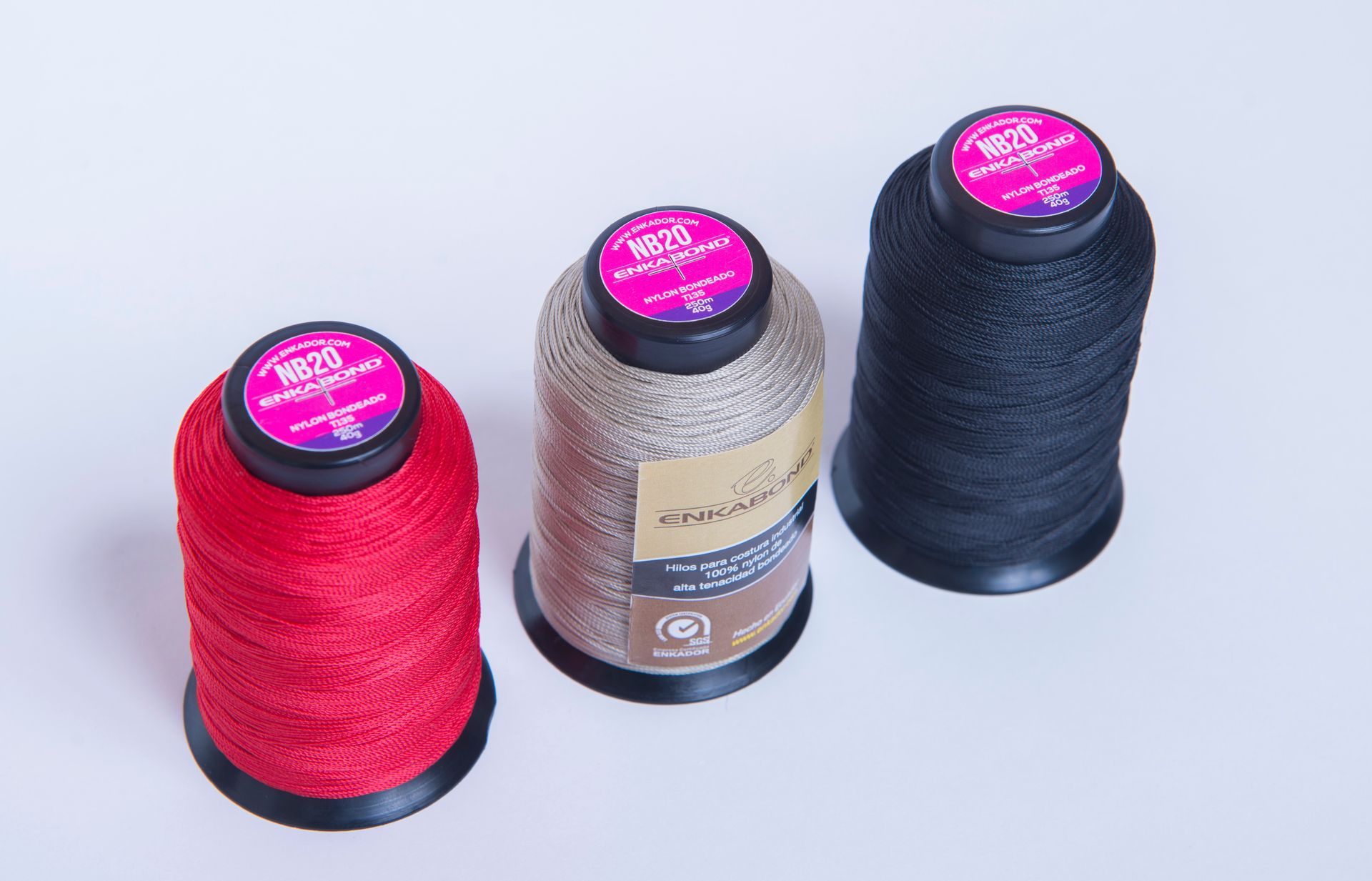 Three spools of thread: red, silver, and dark blue, arranged on a white background.