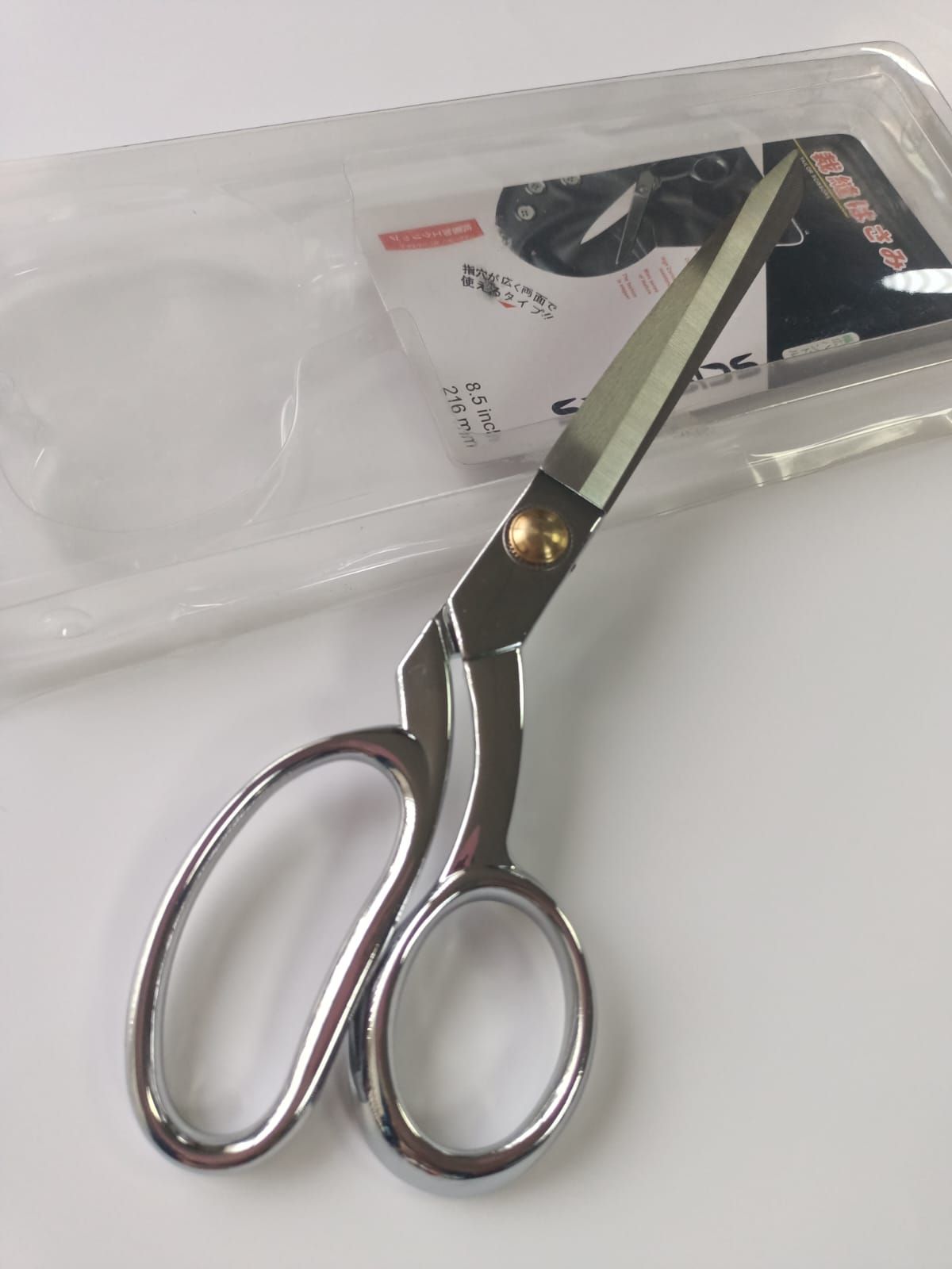 Silver scissors on clear plastic packaging with a white label background