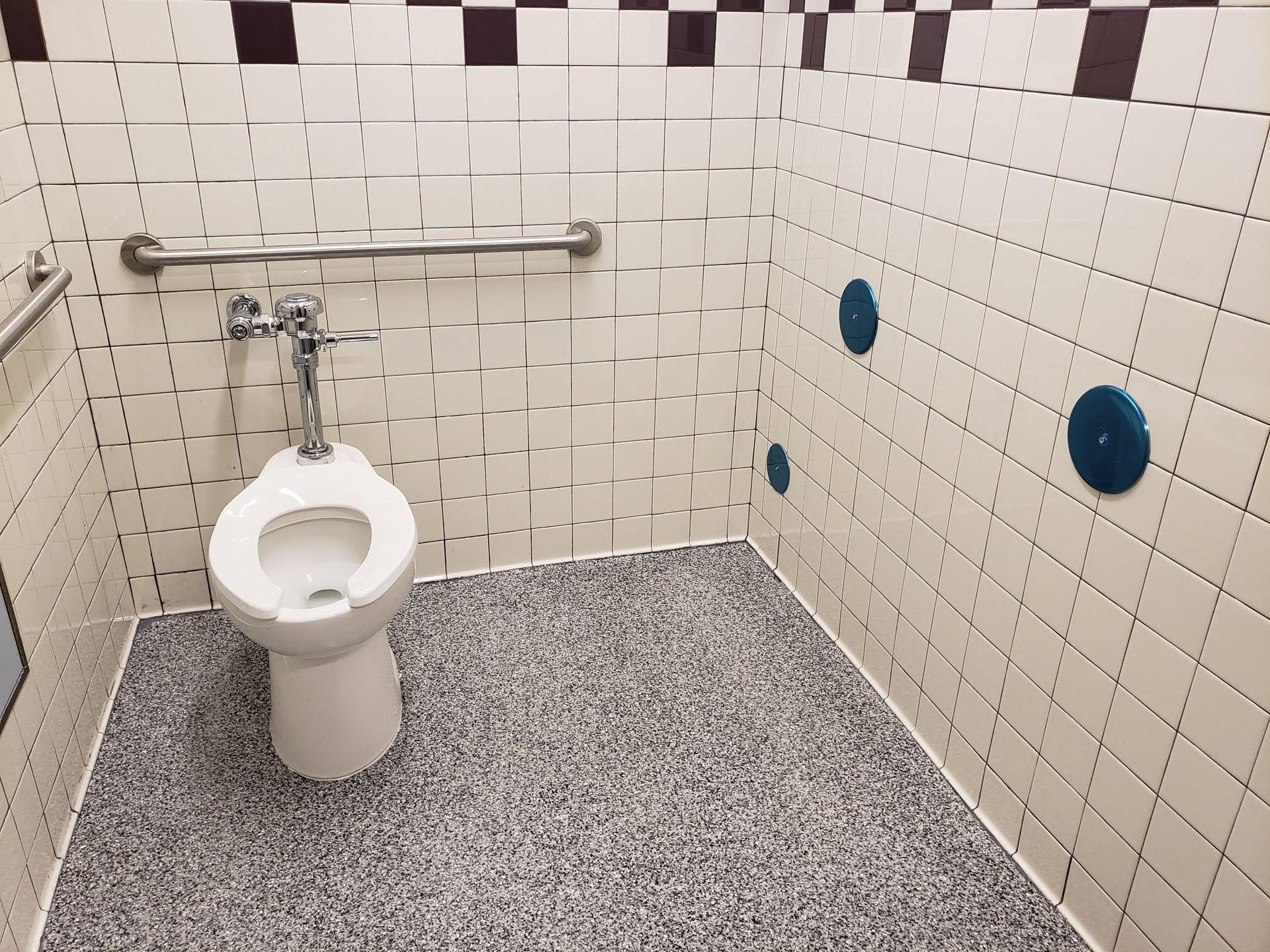 Worker in blue overalls fixing a toilet in a tiled bathroom stall