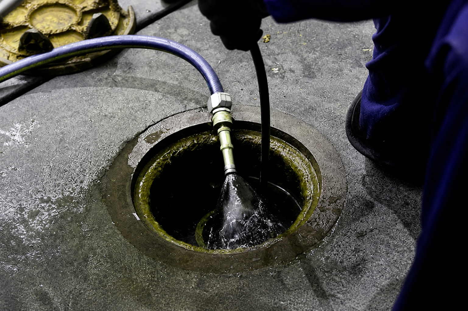 Worker spraying water into a round drain opening on concrete ground