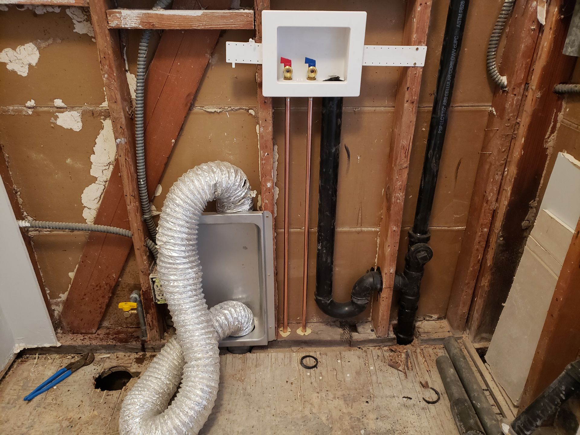 Exposed wall plumbing with silver ducting and a small white wall box in a renovation area