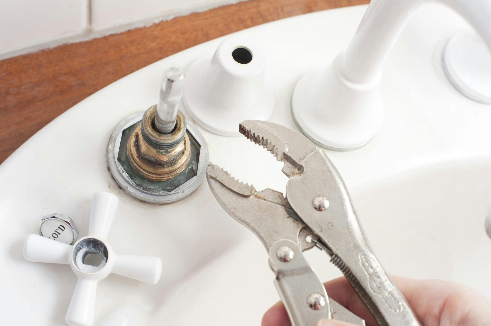 Hand using pliers to remove a corroded faucet valve on a sink with the handle detached