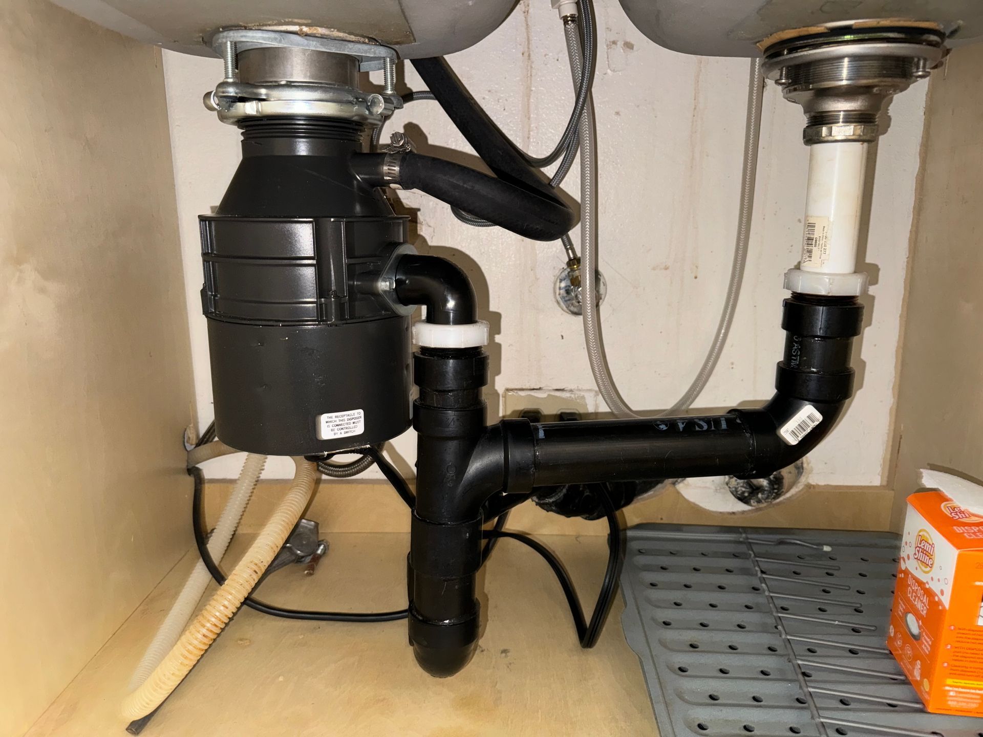 Under-sink plumbing with a black garbage disposal and connected drain pipes in a cabinet