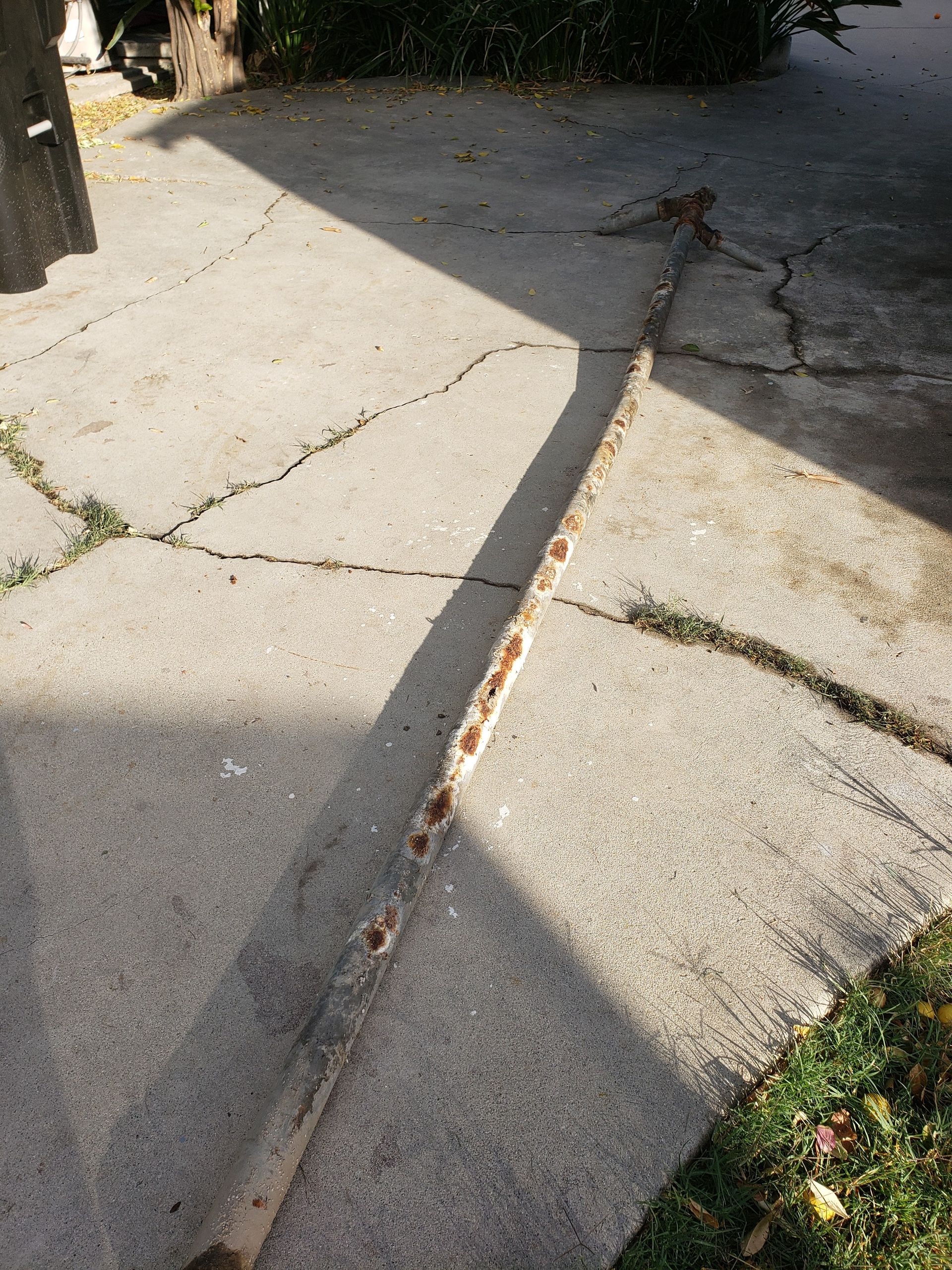 Cracked concrete sidewalk with a long gap filled with debris, lit by sunlight and shadow.