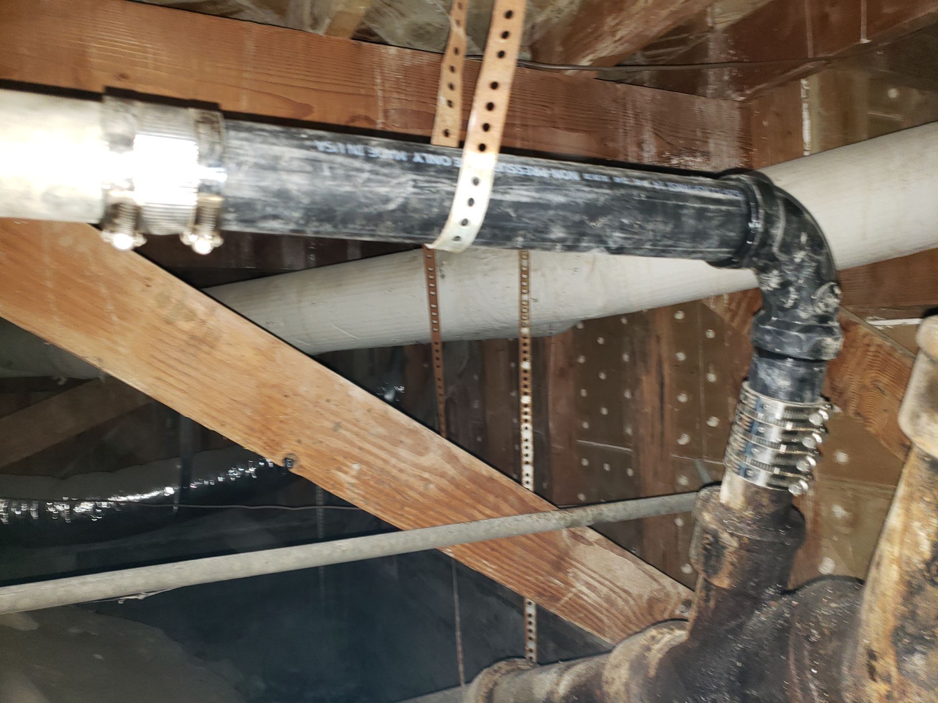 Insulated black ductwork and a taped pipe in an unfinished attic with wooden framing.