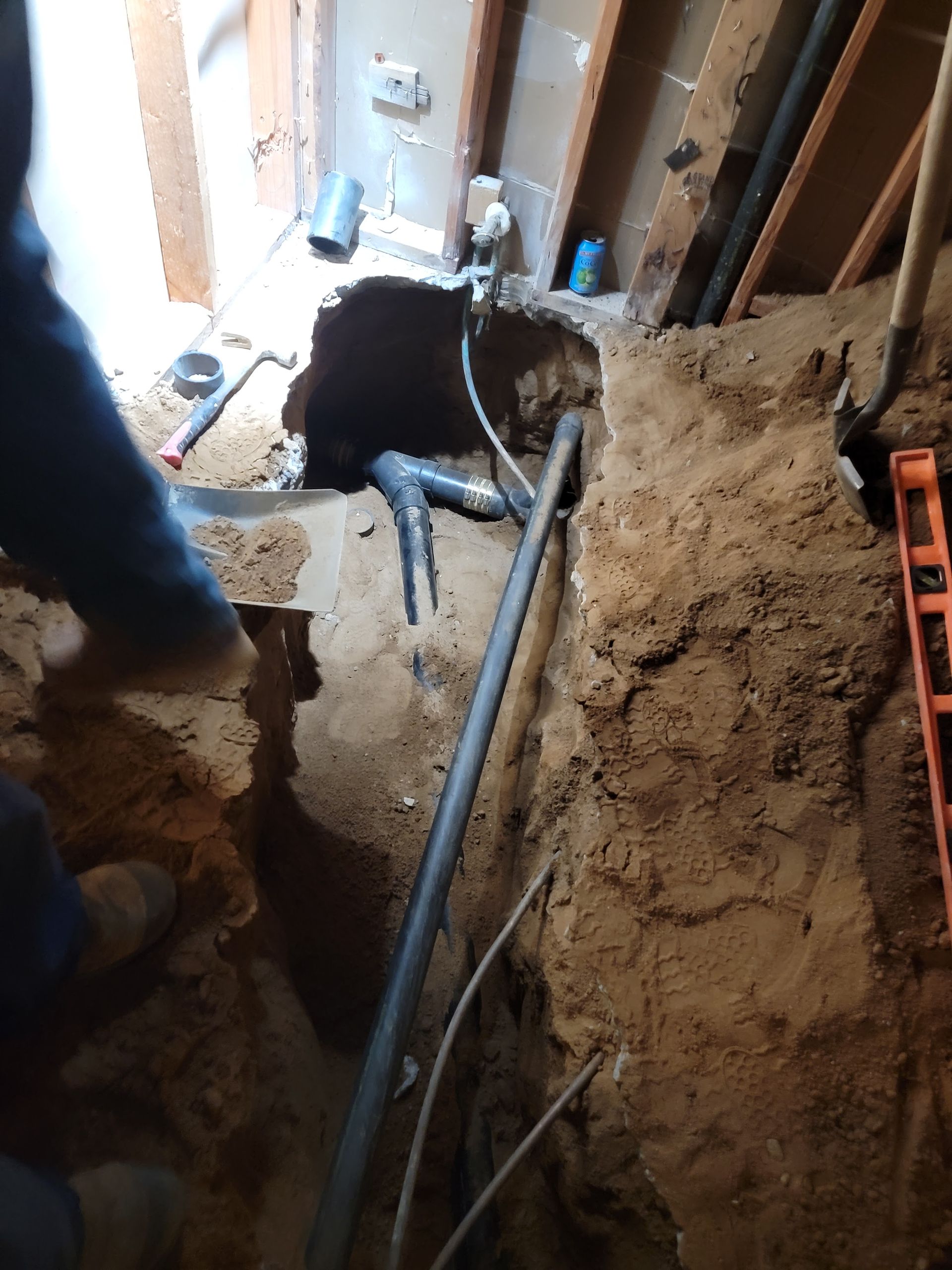 Excavated floor with exposed pipes and dirt beside a wall under repair inside a building