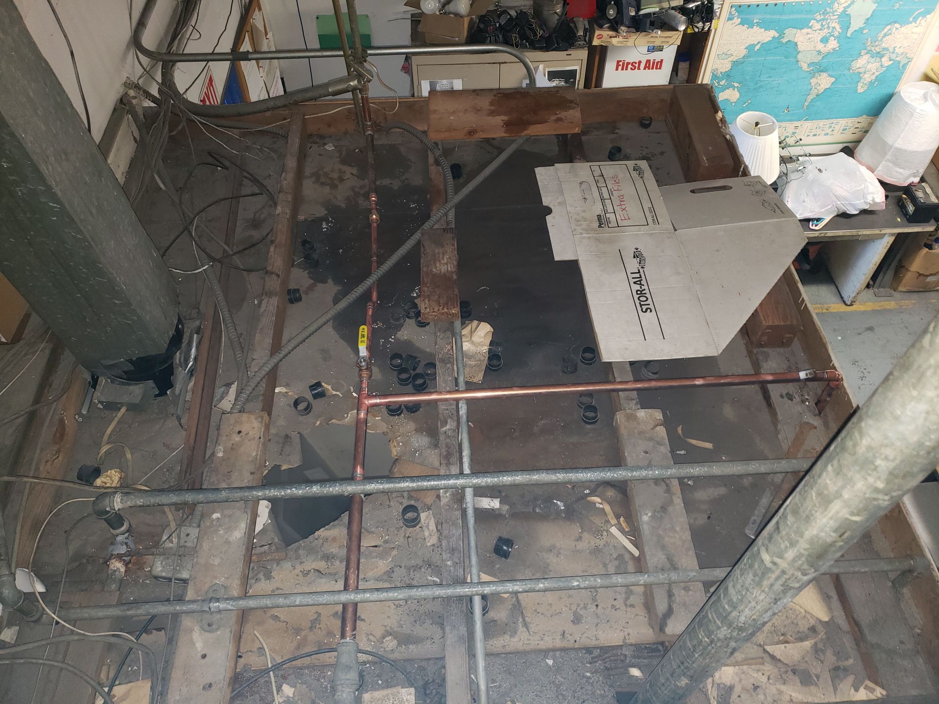 Damaged floor opening with exposed beams and debris in a cluttered room