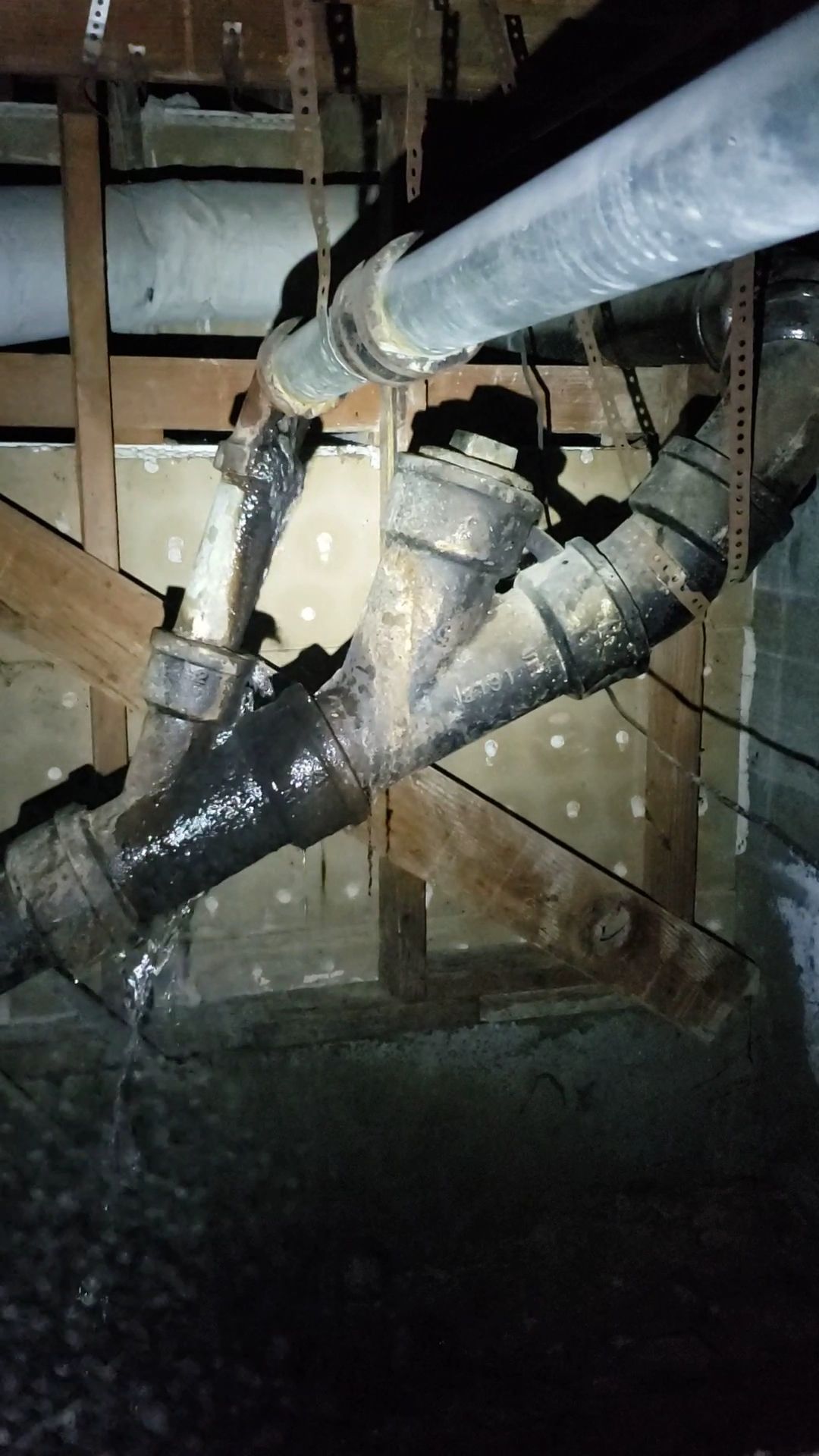 Exposed basement pipes and black insulated ducts crossing a wooden wall cavity