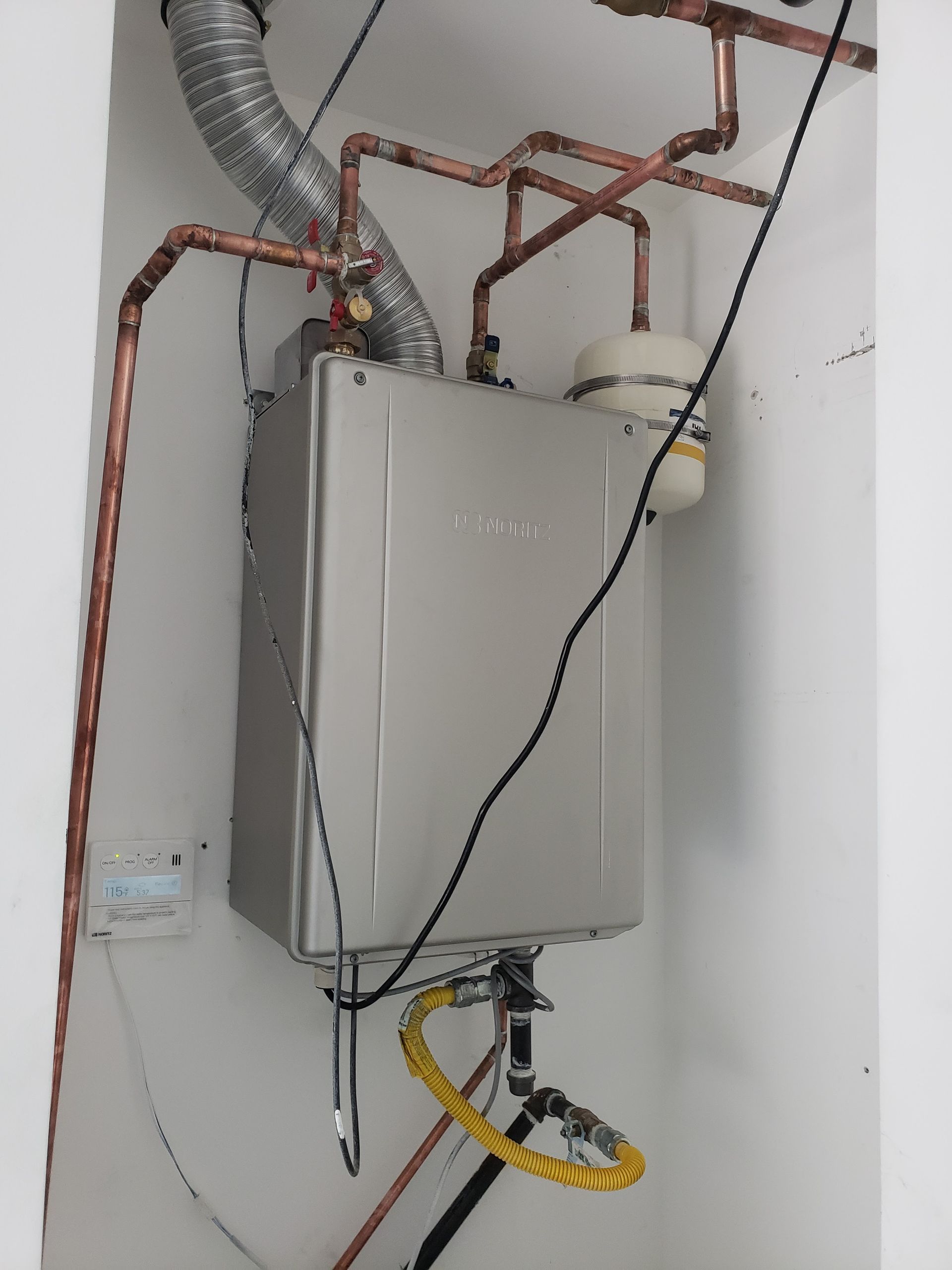 Gray utility box with exposed wiring and metal ducts in a corner of a white room
