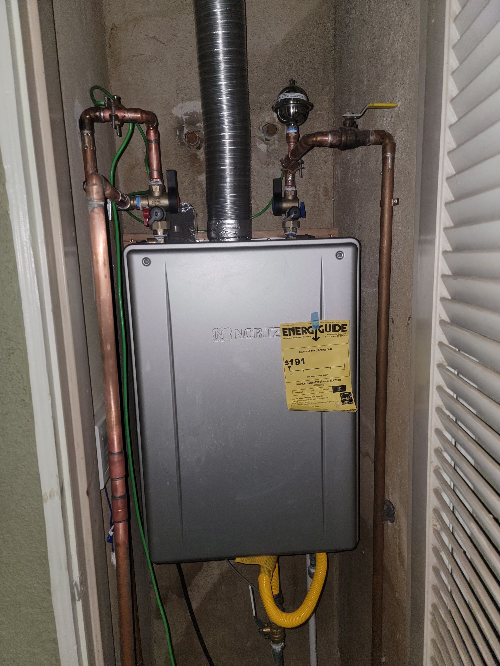 Wall-mounted gas furnace with exposed copper pipes and a yellow service tag in a utility closet