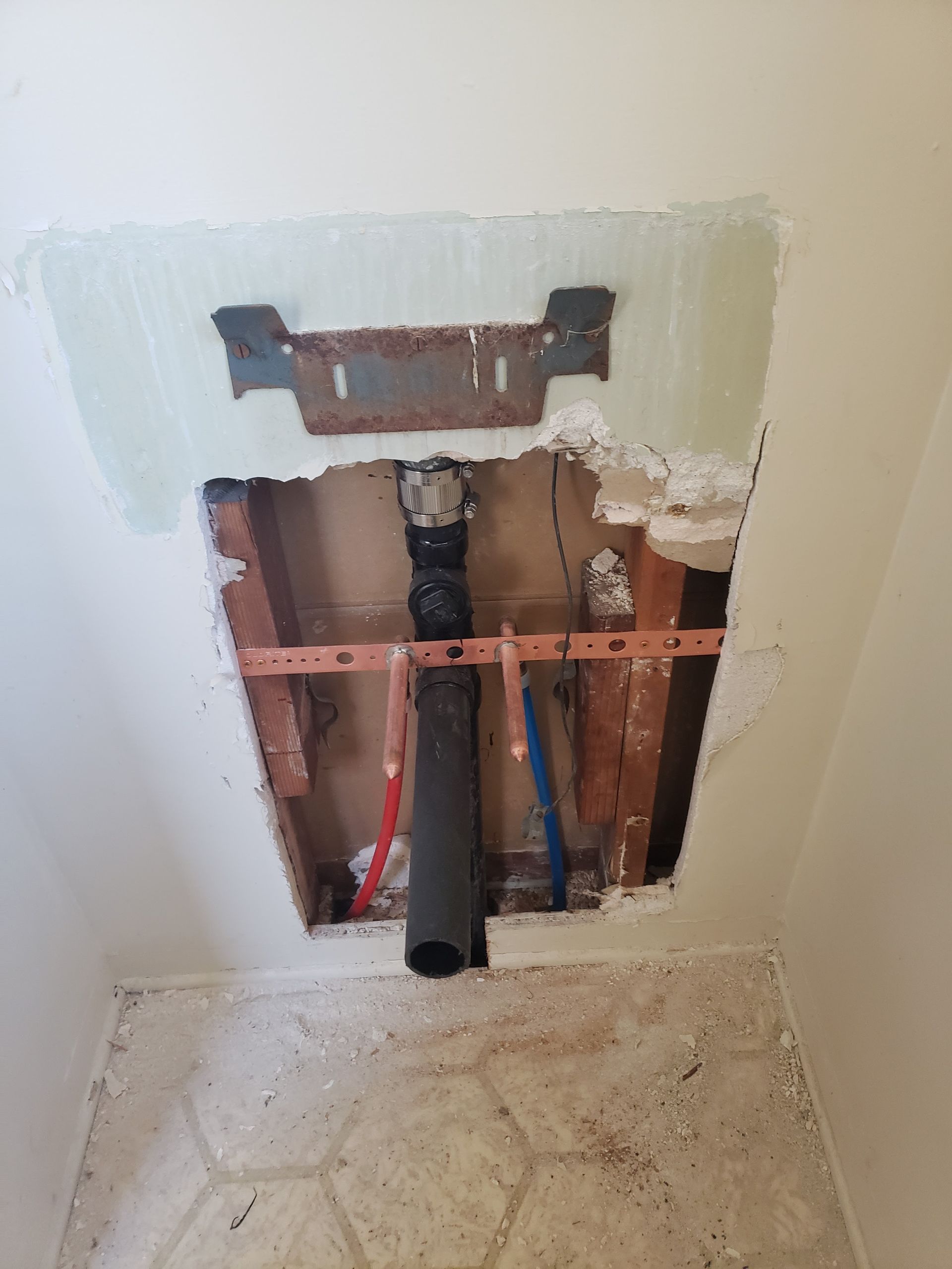 Bathroom wall opening exposing plumbing pipes and studs beneath a sink area