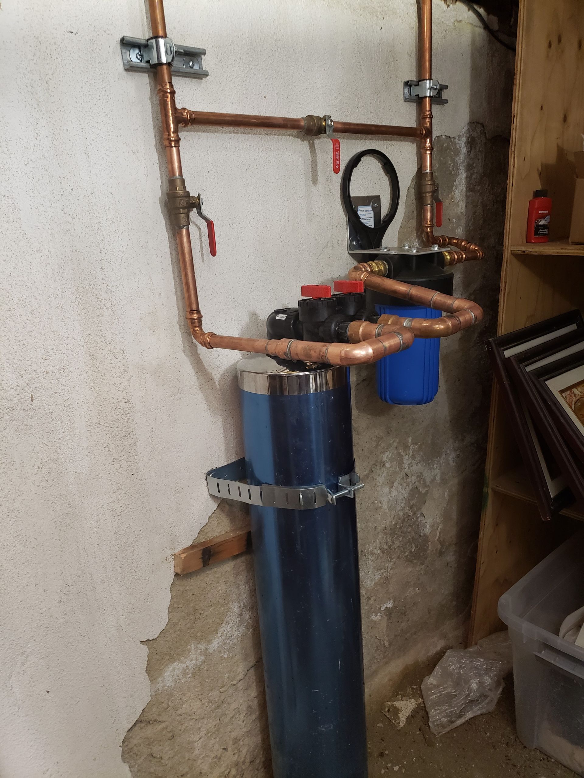 Blue water softener tank with copper plumbing in a utility room, beside a wall and concrete floor