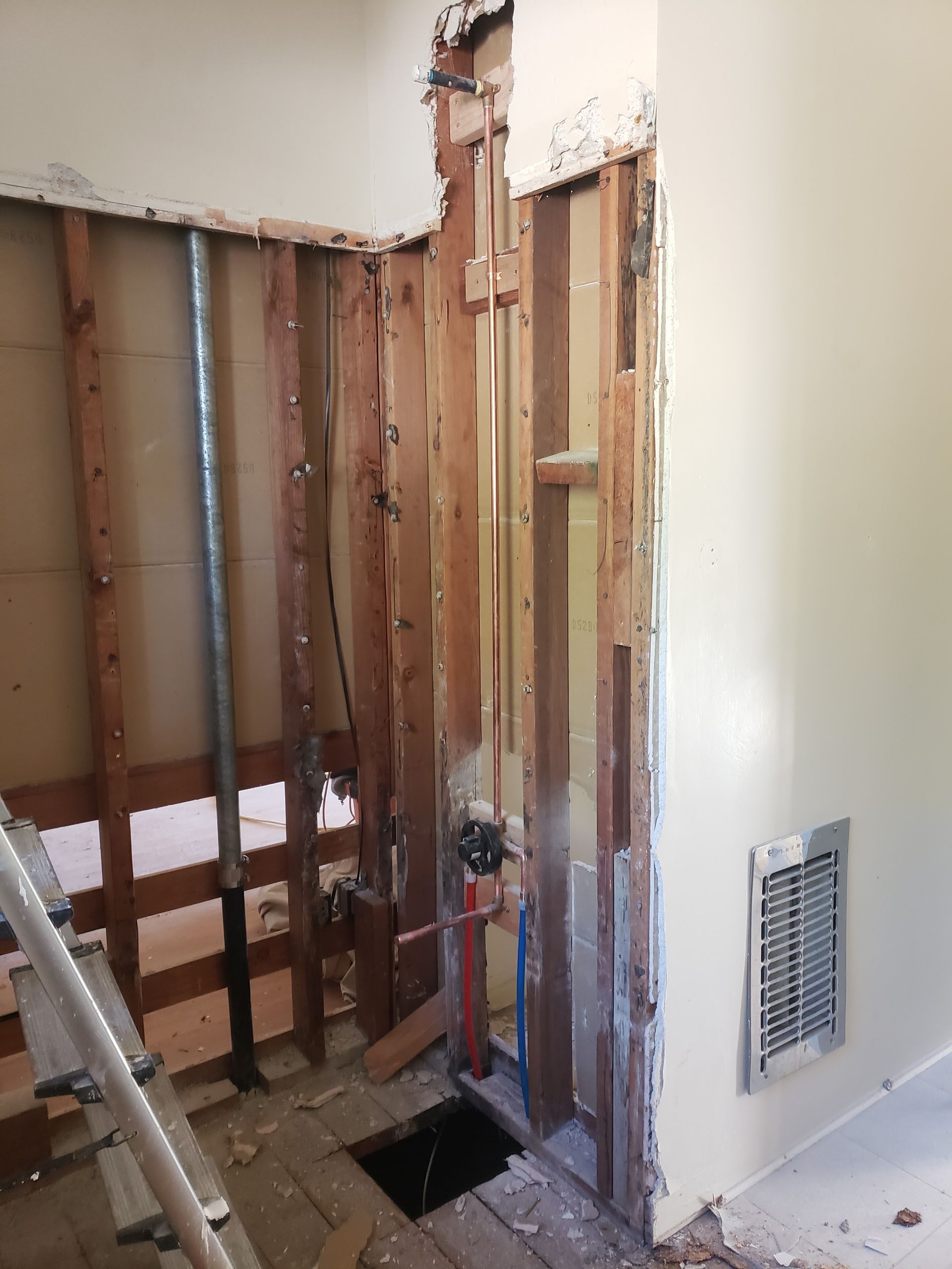 Interior wall under renovation with exposed studs, ladder, and a vent on a white wall