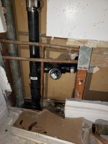 Hands installing a white sink drain and plumbing under a bathroom sink.