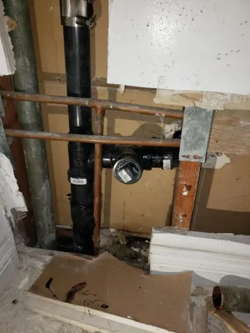 Hands installing a white sink drain and plumbing under a bathroom sink.