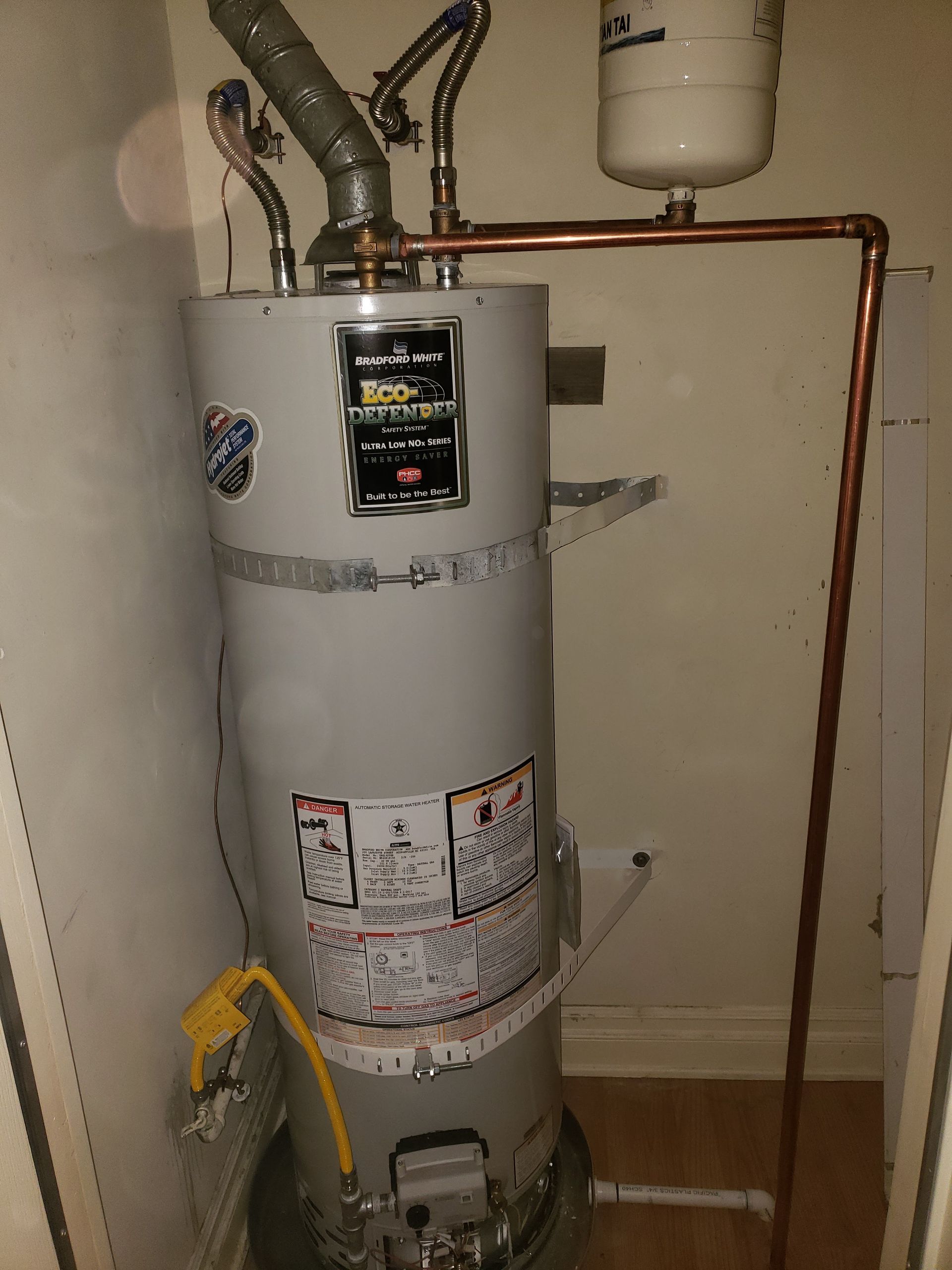 Gray water heater with copper pipes and a yellow gas line in a utility closet