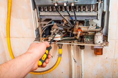 Hand holding a screwdriver near exposed electrical wiring inside a metal control panel