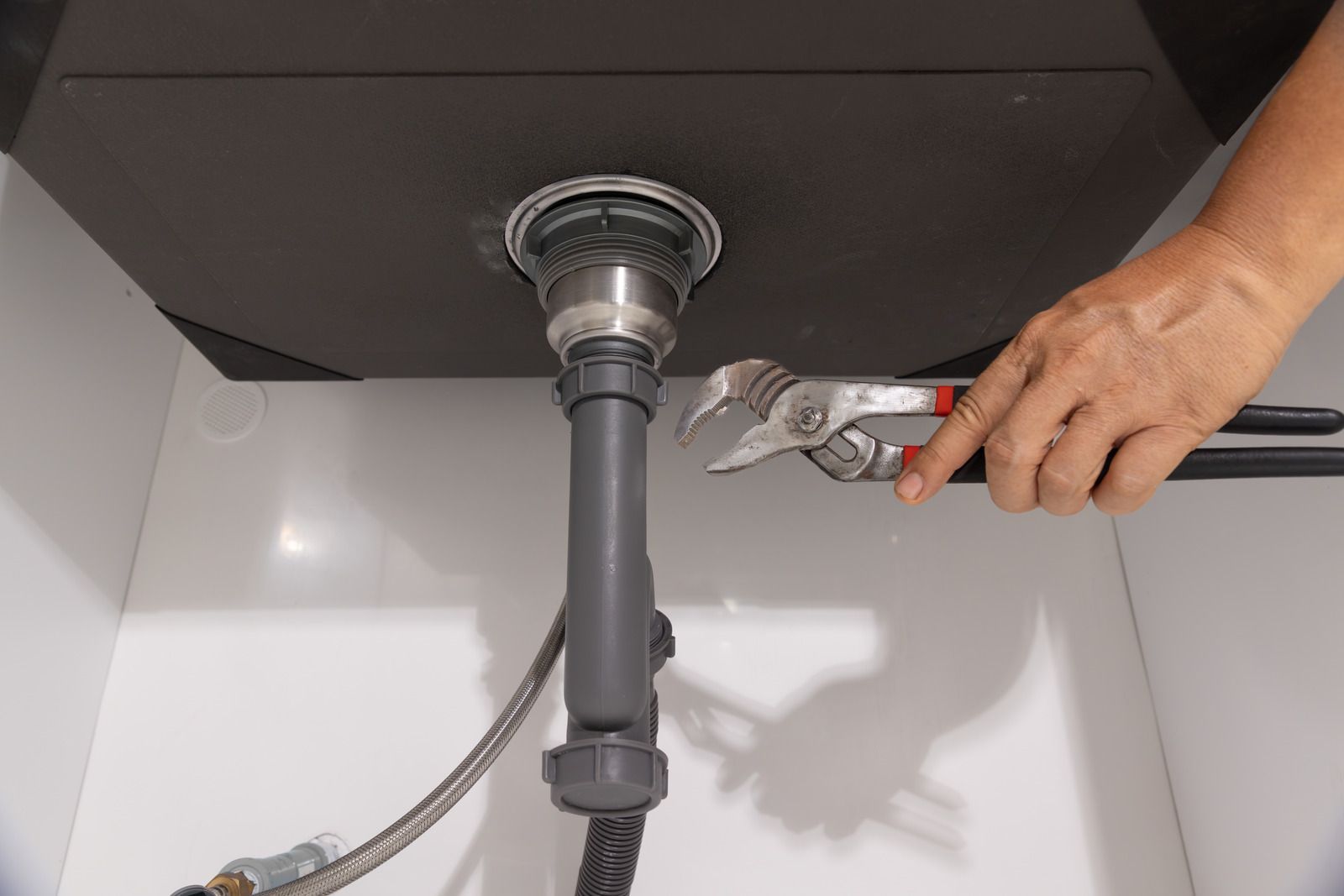 Hand tightening a pipe connection under a sink with adjustable pliers