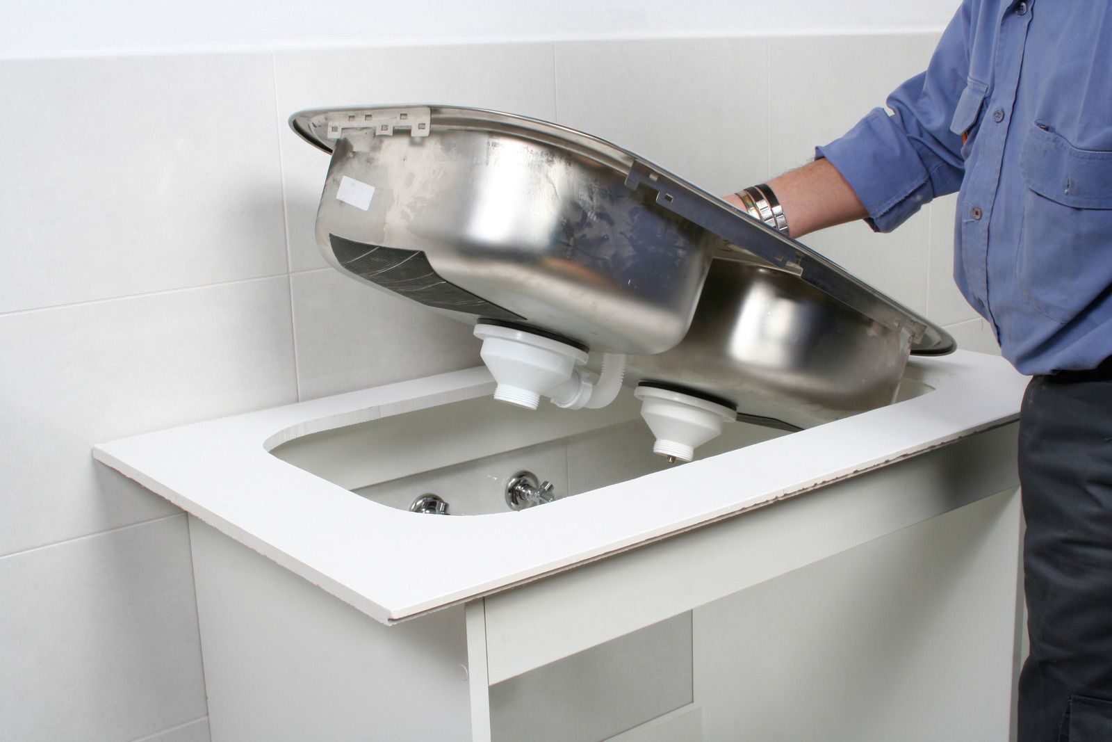 Person lifting a stainless steel sink into a white vanity cabinet cutout