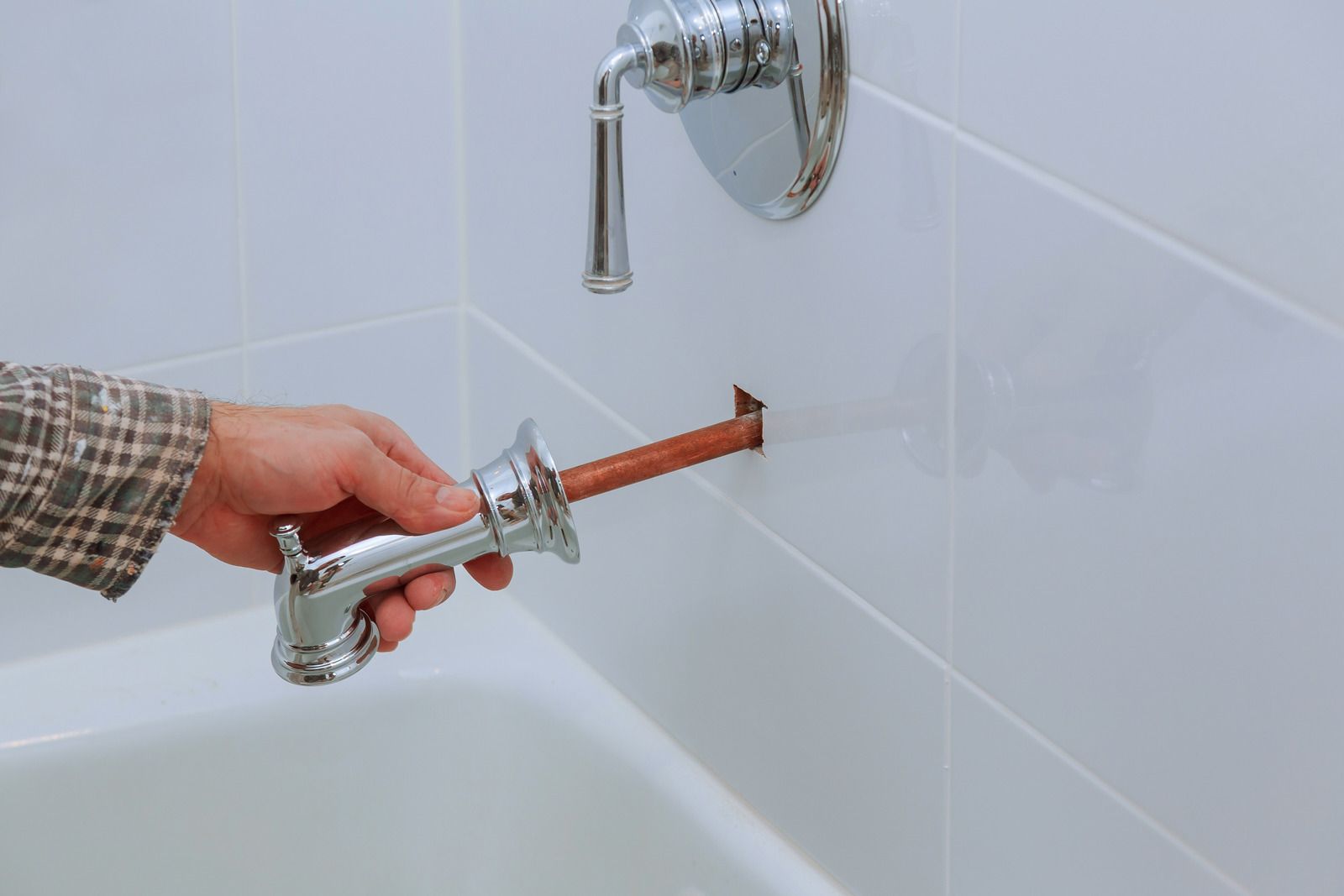 Hand holding a suction-cup tile puller against a white tiled bathtub wall near a chrome faucet