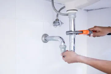 Hands tightening a bathroom pipe with pliers under a sink