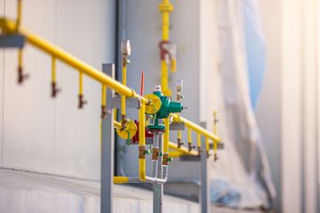 Yellow industrial gas pipes with green valves and gauges along a white wall in a facility