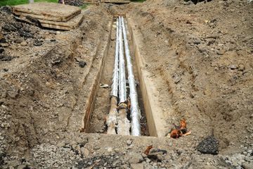 Excavation trench with several white utility pipes laid underground at a construction site