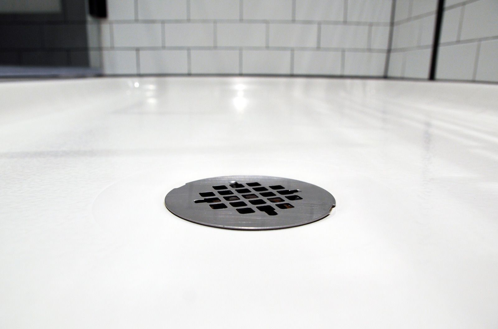 White tiled shower floor with a round metal drain grate in the center