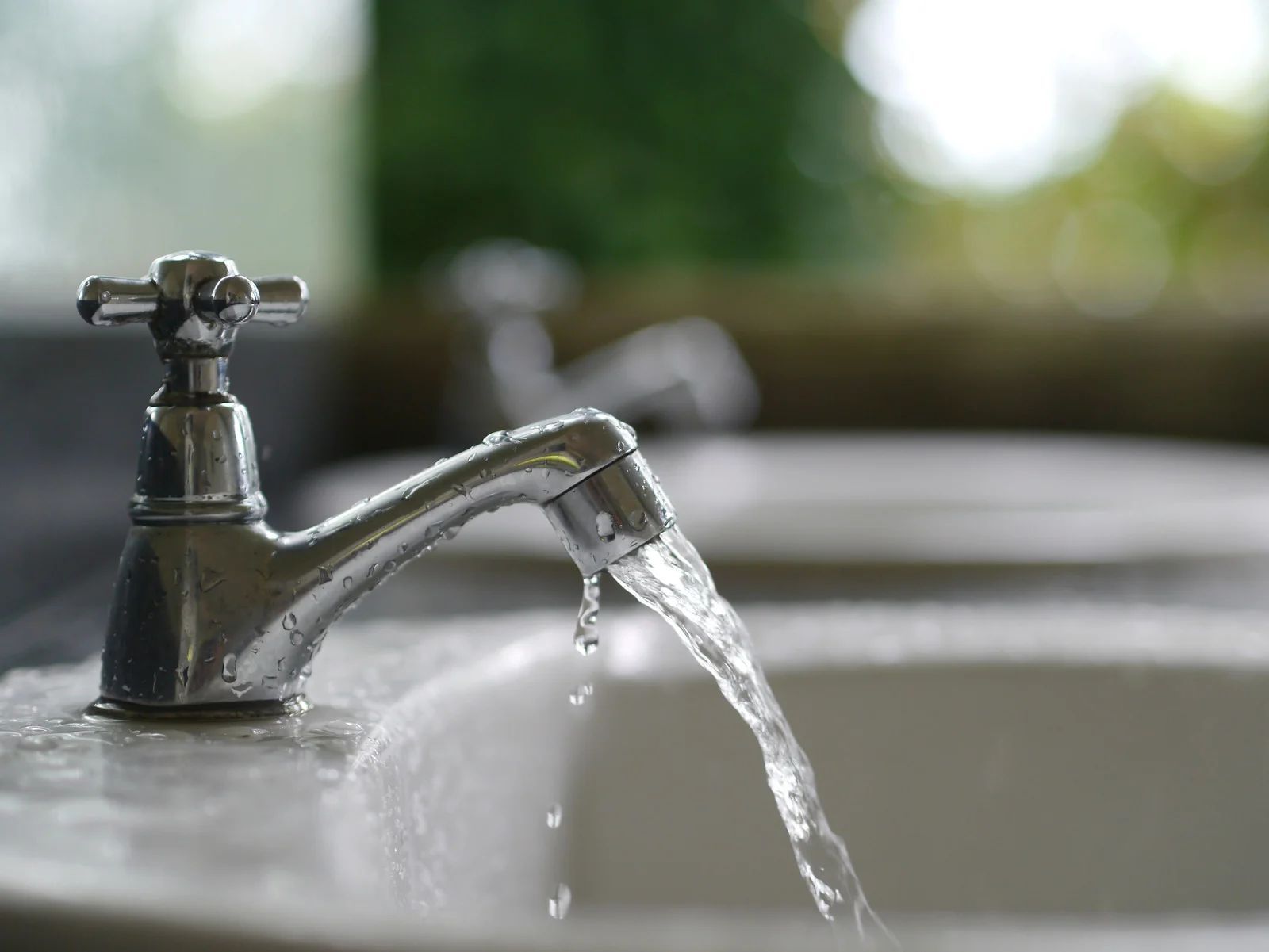 Metal faucet with running water splashing into a sink outdoors