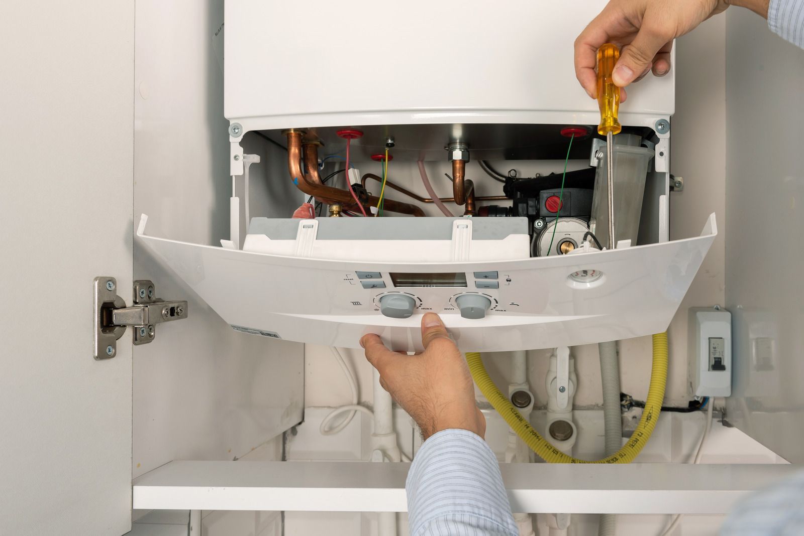 Hands repairing an open wall-mounted boiler with tools and exposed wiring