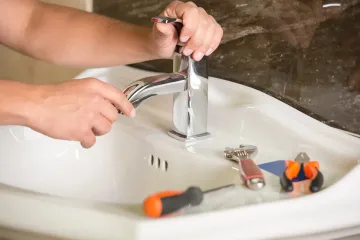 Hands tightening a faucet in a white sink with tools nearby