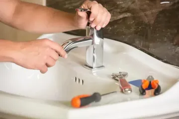 Hands tightening a faucet in a white sink with tools nearby