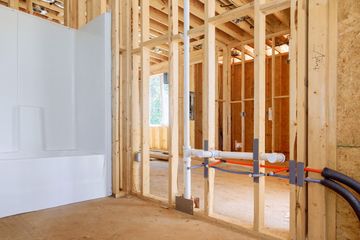 Interior framing of a house under construction with exposed studs, drywall, and plumbing lines