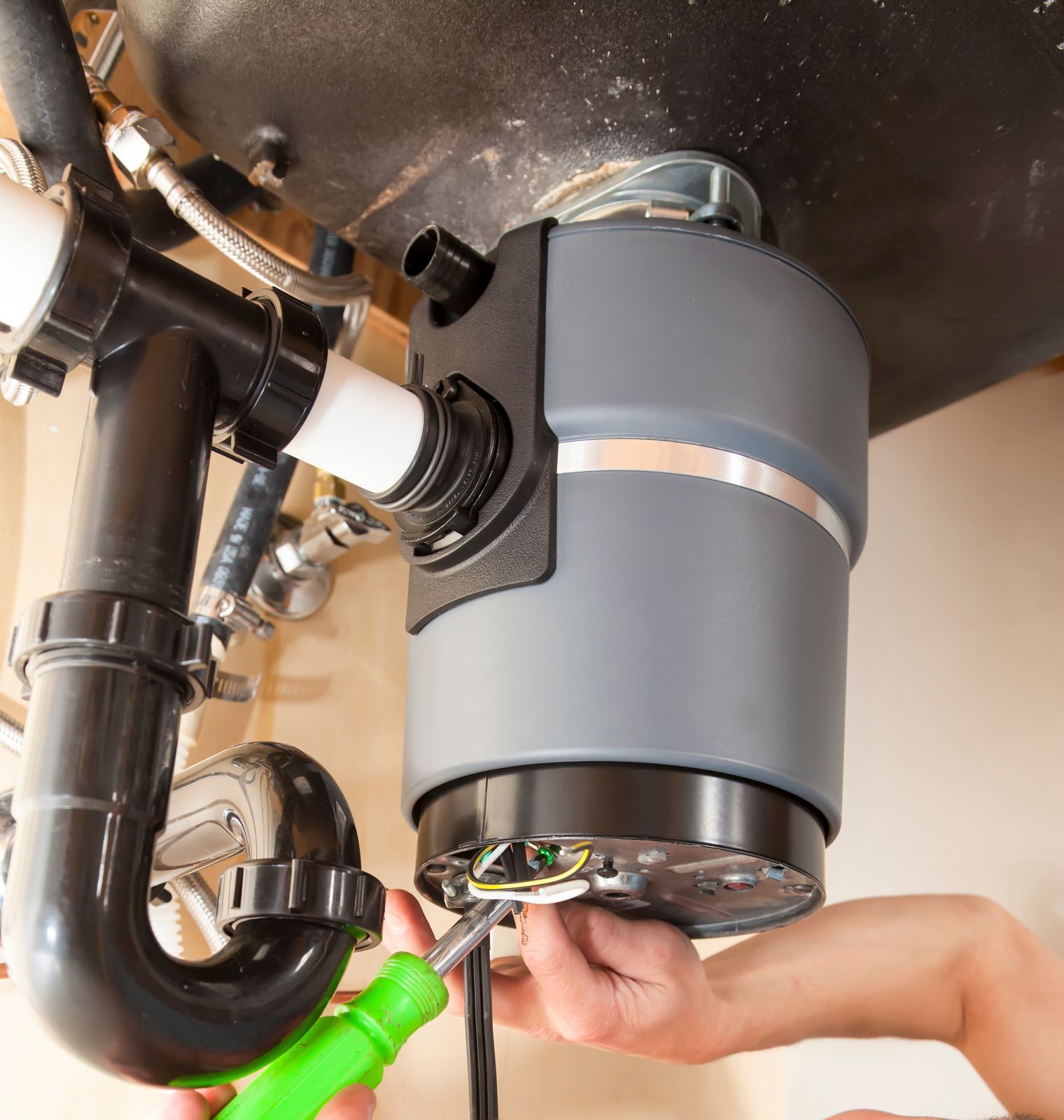 Hand tightening a gray under-sink garbage disposal beneath a black drainpipe