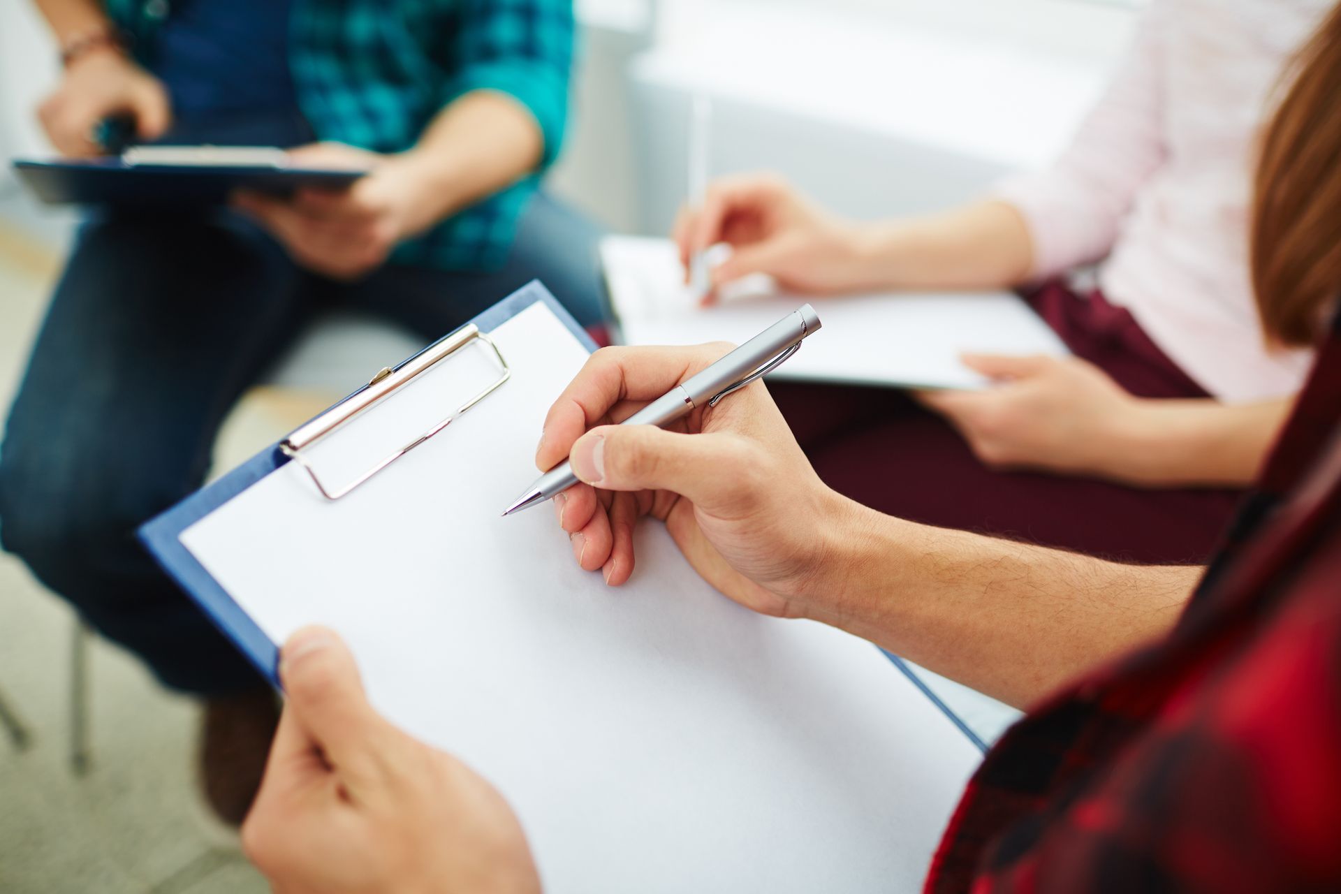 People seated in a meeting, taking notes on clipboards and notebooks.