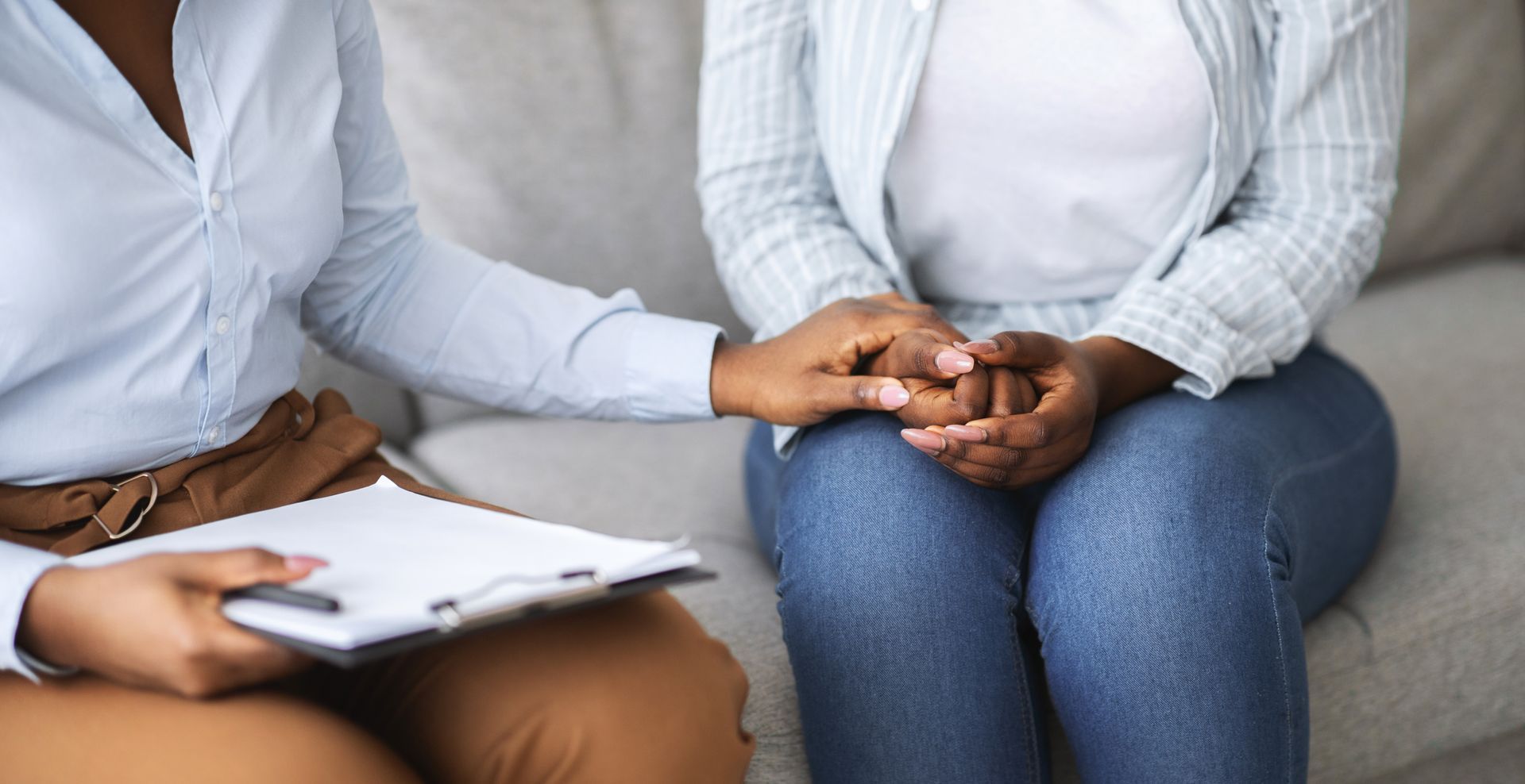 Two people seated on a couch, holding hands during a counseling session with a clipboard nearby