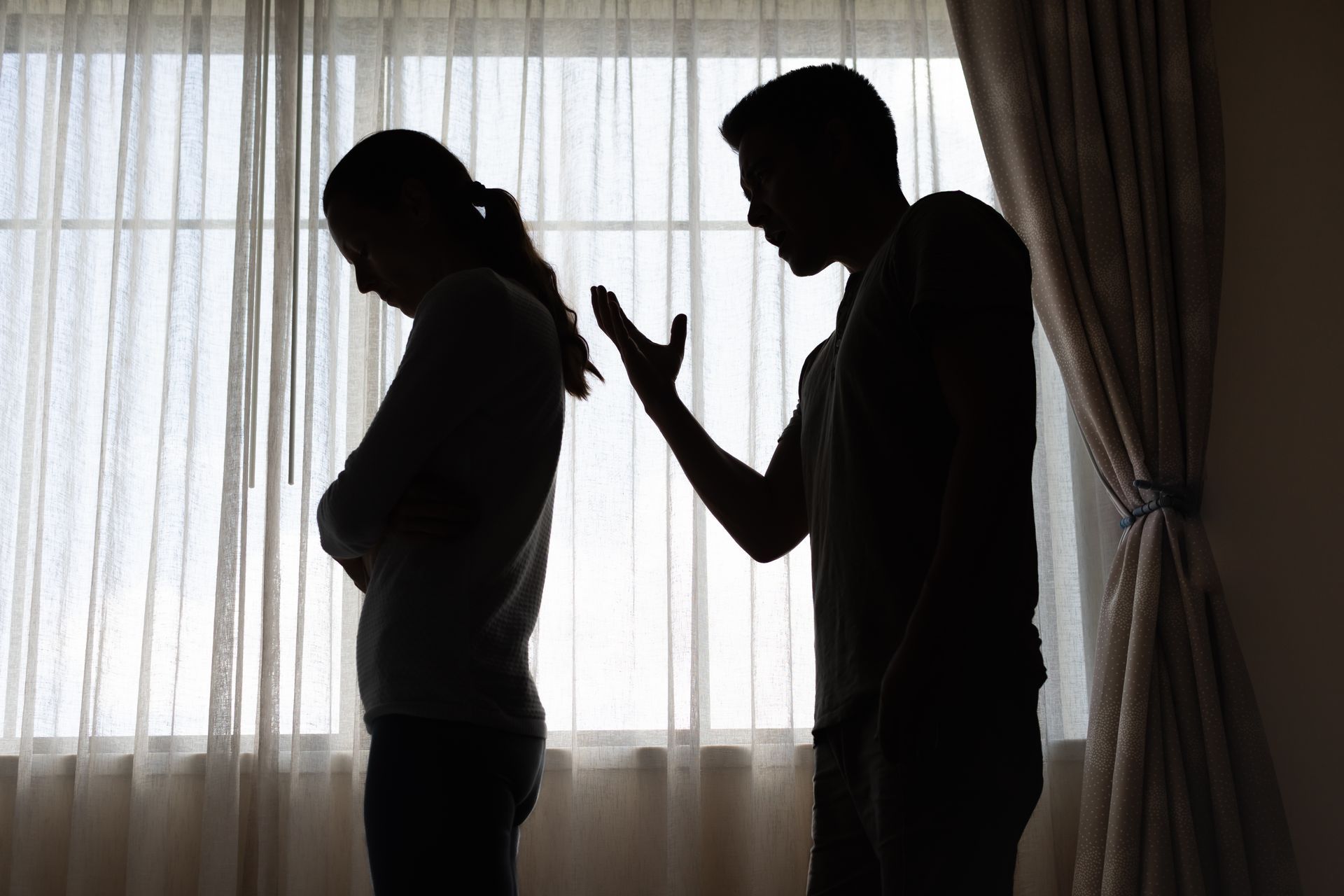 Two silhouetted people standing by a window, one gesturing while the other faces away.