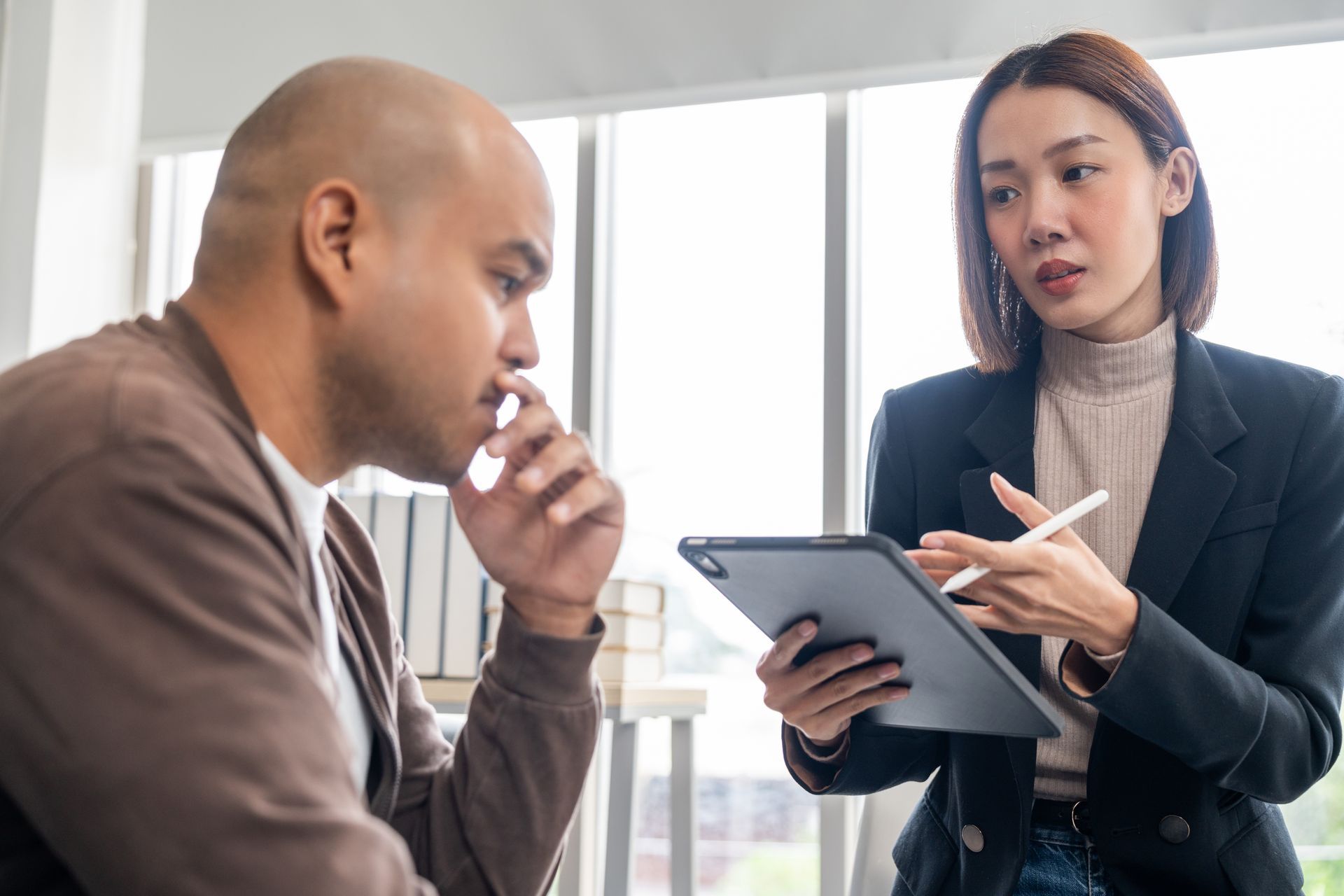 Two people in a bright office discuss notes, one holding a tablet and pen
