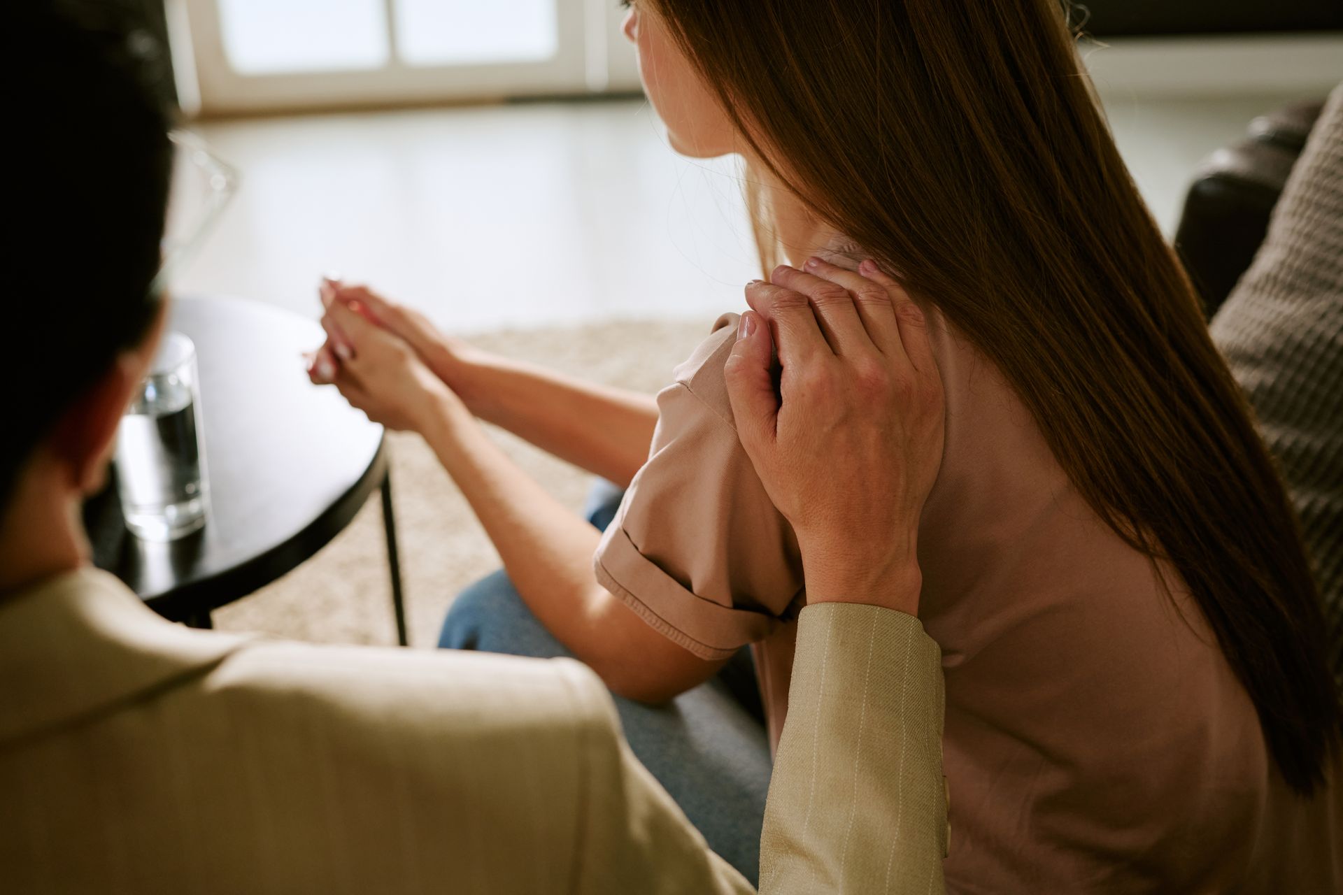 Person comforting another person seated on a couch in a bright living room