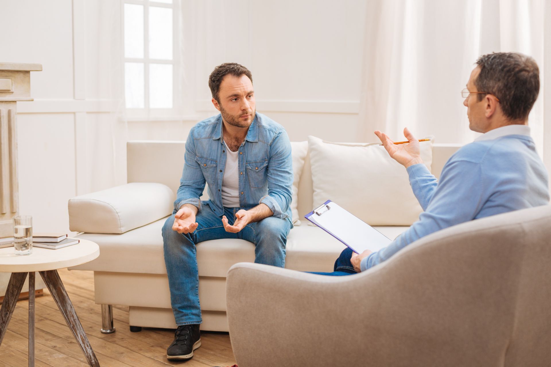Two men talking in a bright living room during a counseling session