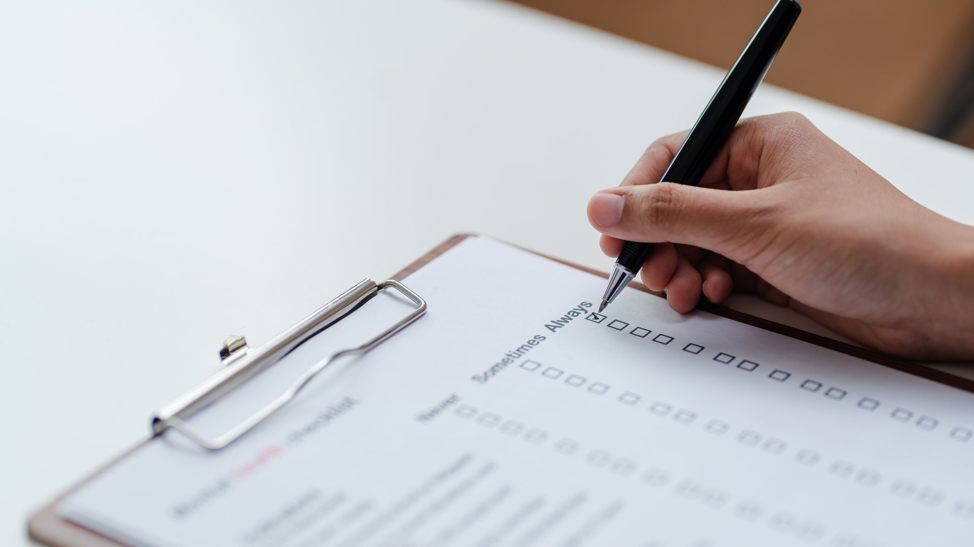 Hand filling out a form on a clipboard with a pen, close-up on a desk