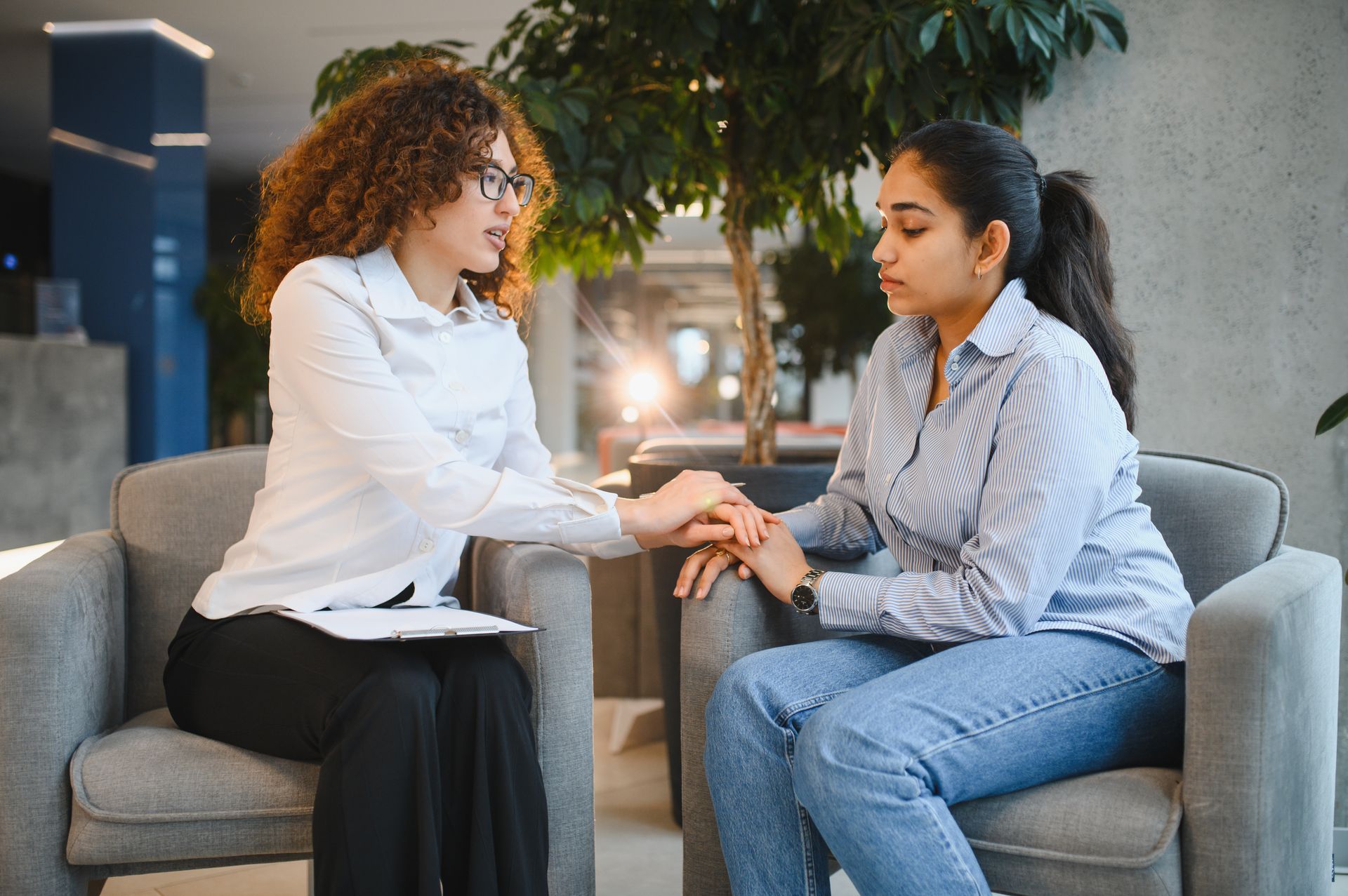 Two people sitting on a sofa, holding hands and talking in a cozy indoor setting.