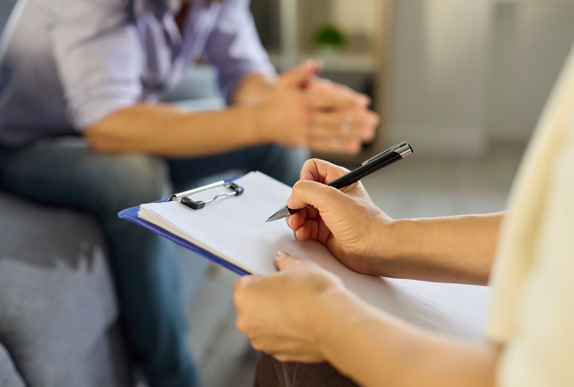 Therapist taking notes on a clipboard while seated opposite a patient in a 상담 room