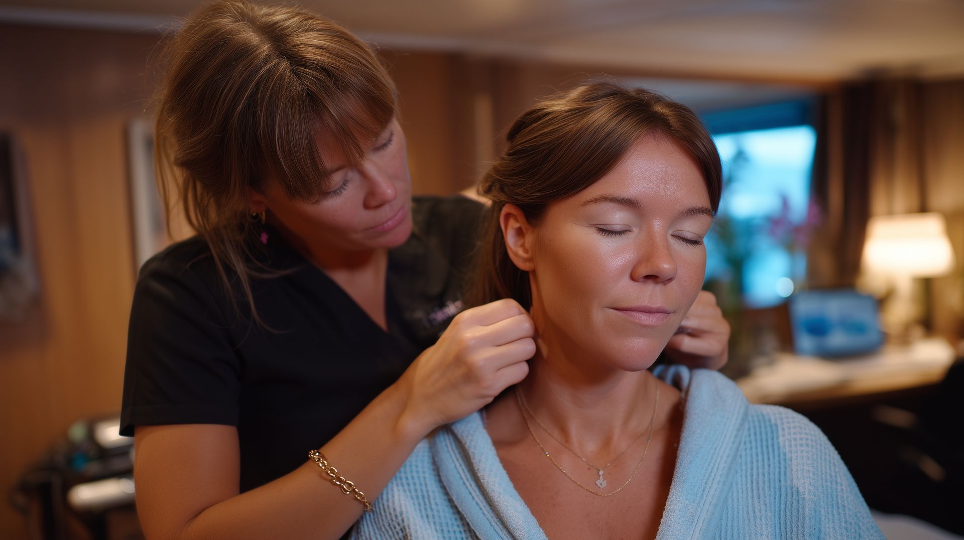 Two women in a warmly lit room, one applying makeup to the other’s face