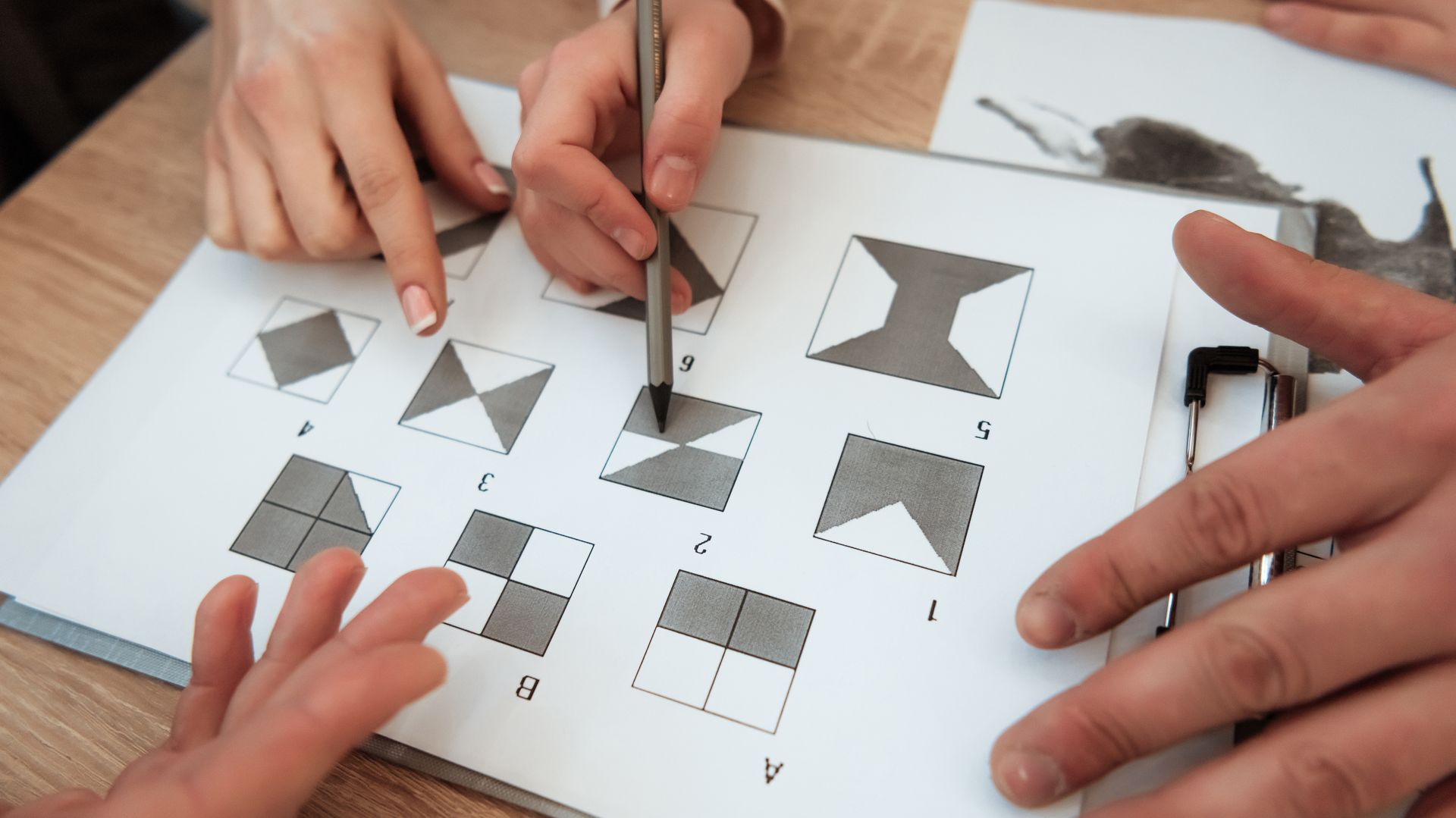 Hands solving a paper puzzle with cut-out geometric shapes on a desk