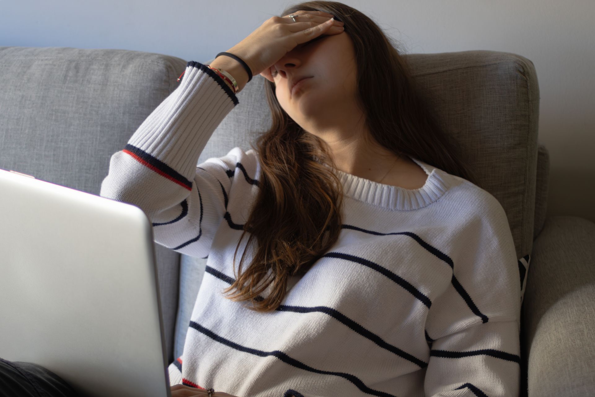 Person on a couch with a laptop, hand over face as if tired or stressed.