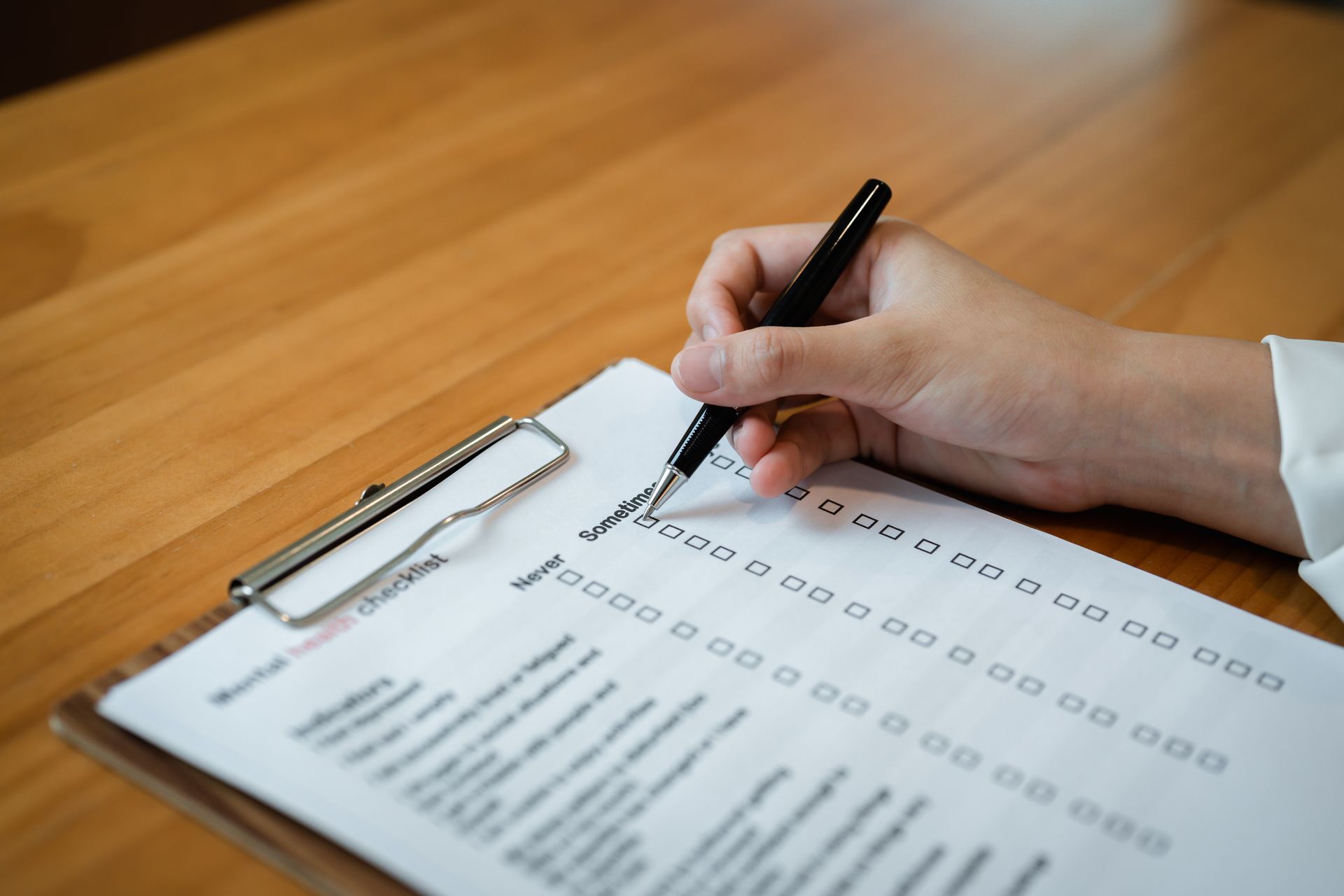 Hand filling out a checklist on a clipboard at a wooden desk